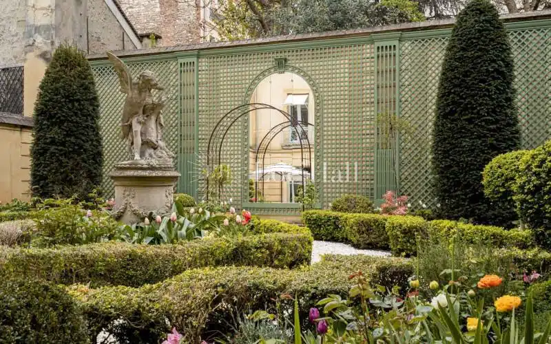 Le jardin à la française de l’hôtel de Bouillon avec un gros plan de sa statue et du mur du fond avec son grand miroir décoratif.